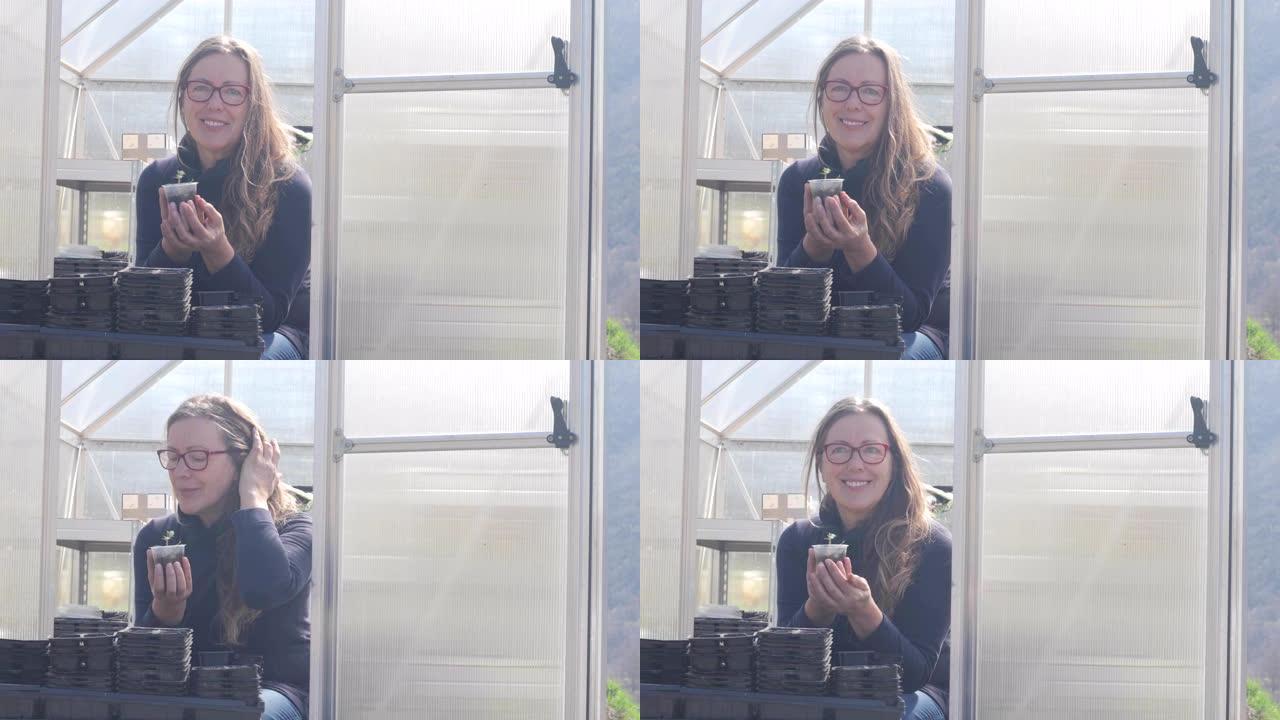 微笑的成熟女人在温室前抱着番茄苗