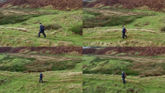 在苏格兰西南部偏远农村地区，一名活跃的高级男子在粗糙的未耕地上行走的高角度视图