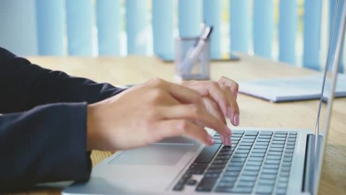 人的手在办公室背景的笔记本电脑上工作。办公室里的一名年轻女子在键盘上拨打文档。快速工作。