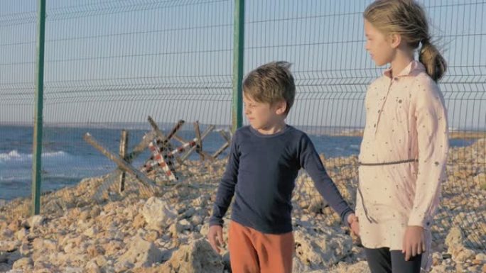 两个贫穷的难民儿童站在战争冲突地区的海边。男孩和女孩等待被救出