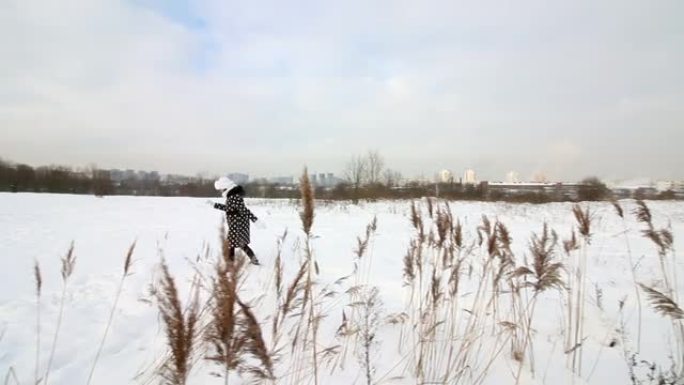 女孩走过冬天的荒原。在深雪中行走。在又高又干的草丛中。
