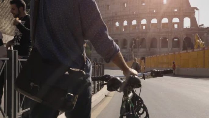 年轻的潮人在阳光明媚的日子里骑着自行车在罗马斗兽场散步慢动作摄影车steadycam