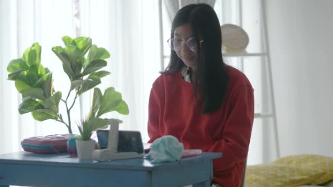 穿着红色毛衣学习在线课程的亚洲女孩新型冠状病毒肺炎在家上学和新常态概念。