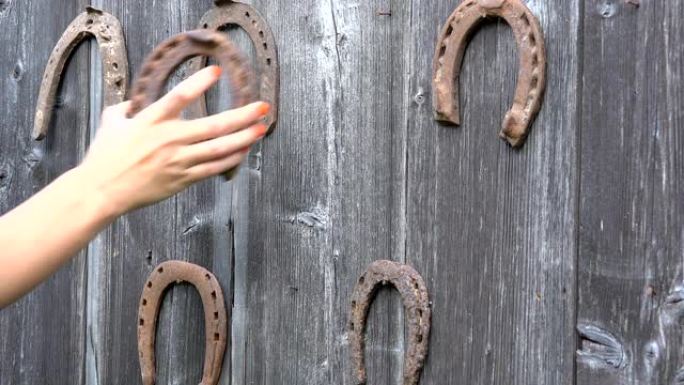 女孩手把复古生锈的马蹄铁放在古老的木制乡村房屋墙上。特写。4K