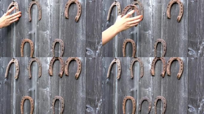 女孩手把复古生锈的马蹄铁放在古老的木制乡村房屋墙上。特写。4K