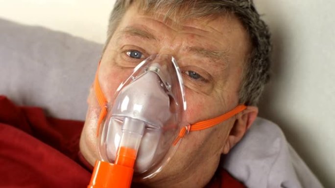 生病的中年男子躺在床上通过氧气面罩呼吸。