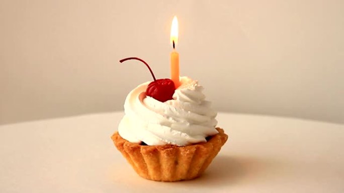 饼干篮子上有白色糕点奶油、红色鸡尾酒樱桃和一支燃烧的生日蜡烛
