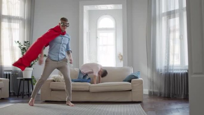 父亲和儿子在公寓里玩游戏。穿着红色斗篷和眼镜的爸爸描绘了超人。