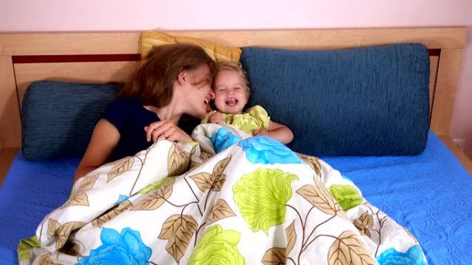 笑着的母亲和蹒跚学步的女孩在床上玩耍