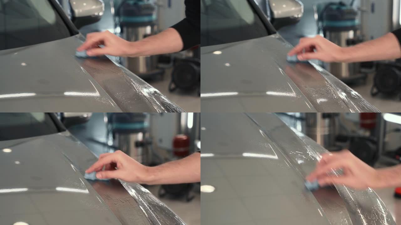 工人在汽车上施加保护层或涂层之前，用蓝色粘土手工清洁车身以进行清洁。汽车细节概念