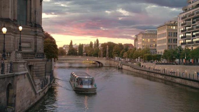 船上有游客在柏林博物馆岛附近的河上航行。首都中心的日落。粉色五彩云。房子里灯亮了。慢动作