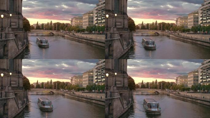 船上有游客在柏林博物馆岛附近的河上航行。首都中心的日落。粉色五彩云。房子里灯亮了。慢动作