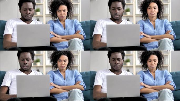非洲男子在生气的女友坐在一边时使用笔记本电脑