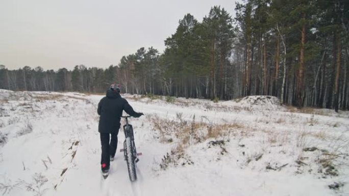 专业极限运动员骑自行车的人在户外用胖自行车行走。骑自行车的人走在冬天的雪林里。男子戴着头盔和眼镜的大