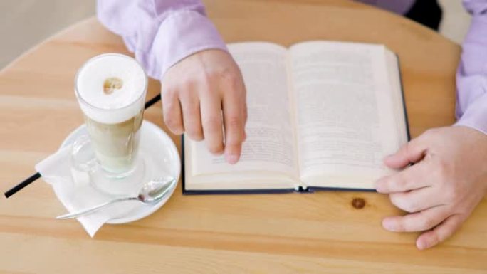 男人正拿着一杯卡布奇诺咖啡坐在咖啡馆里的手指上看书