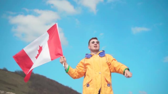 一个穿着黄色夹克，蓝色牛仔裤和眼镜的年轻人站在山上，举着加拿大国旗