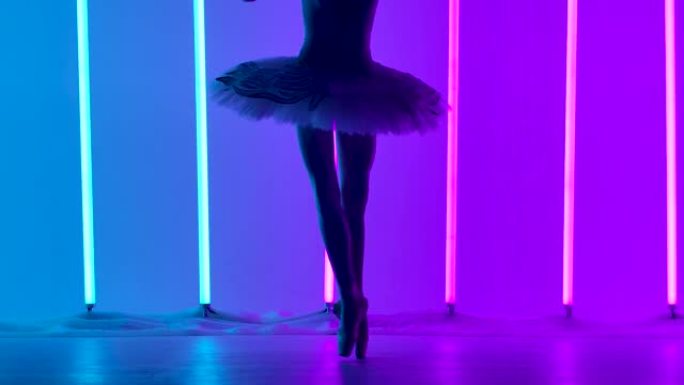 优雅勤奋的芭蕾舞演员穿着白色连衣裙和尖头鞋在明亮的霓虹灯的背景下跳舞古典芭蕾舞。剪影。Tip脚的舞者