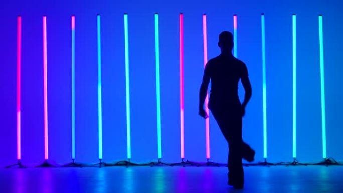 在明亮的彩色霓虹灯的背景下，一个年轻人在工作室里跳舞伦巴舞的黑暗剪影。这个家伙制定了舞蹈，步骤，转弯