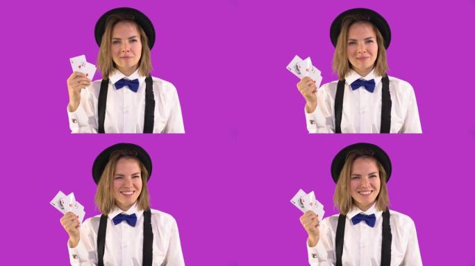 穿着白衬衫，帽子和领结的副主持人女孩表现出扑克牌和微笑。四张王牌，一个女孩眨眨眼。紫罗兰色背景