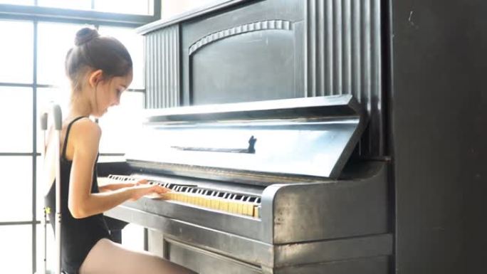4k视频选择性拉移焦点中景，年轻漂亮的小女孩穿着黑色紧身衣坐在工作室玻璃墙前的平板电脑上弹钢琴。