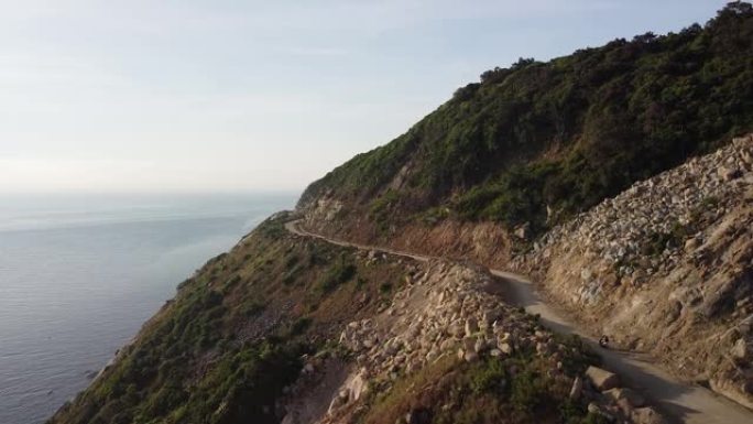 在危险的沿海悬崖边道路上驾驶摩托车的驾车者的鸟瞰图。