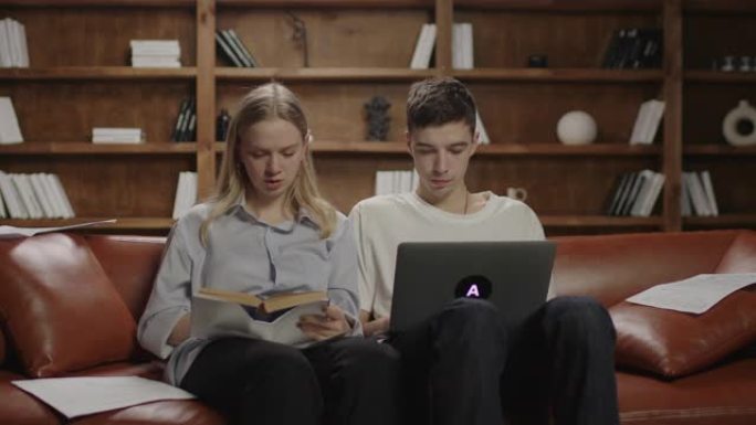 两名20多岁的学生写论文，女性口述书中的信息，男性在笔记本电脑上打字。学生在沙发上的团队合作。