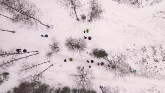 成人和儿童用充气雪橇在树木之间爬山。
