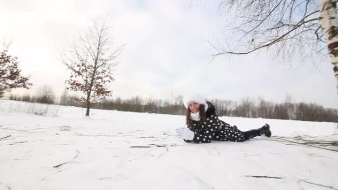 女孩躺在山脚下的雪地里。女孩爬上一座白雪覆盖的小山，坐在雪橇上，滑到山底。