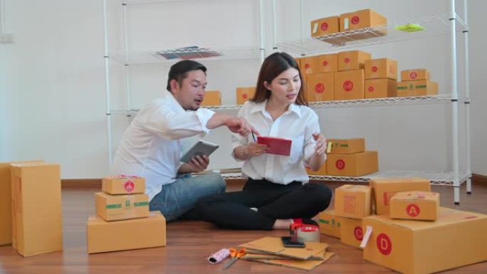 东南亚男女从平板电脑上获得好消息。家庭企业家在自己的工作中检查包裹箱在家购物在线业务