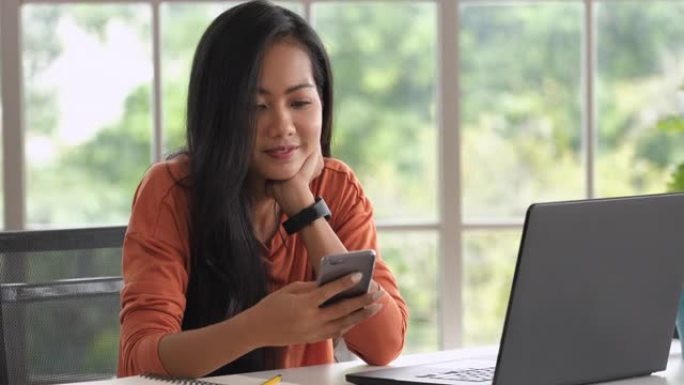 亚洲女性在家中使用笔记本电脑时发短信。新的正常办公室生活方式