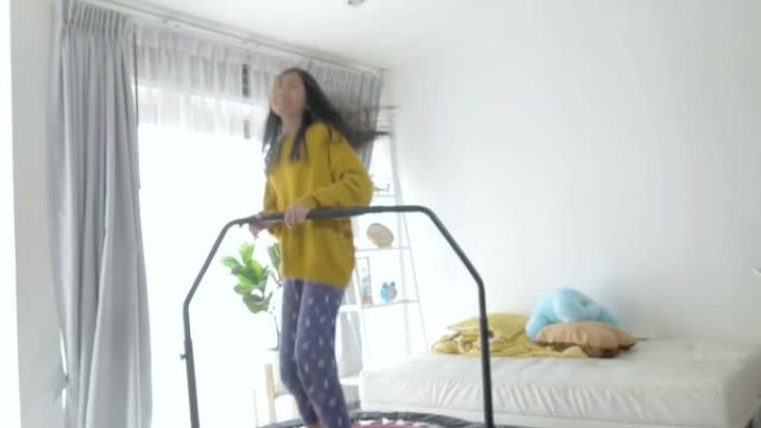 快乐的亚洲女孩在家里跳上迷你蹦床附近的窗户，呆在家里活动理念。