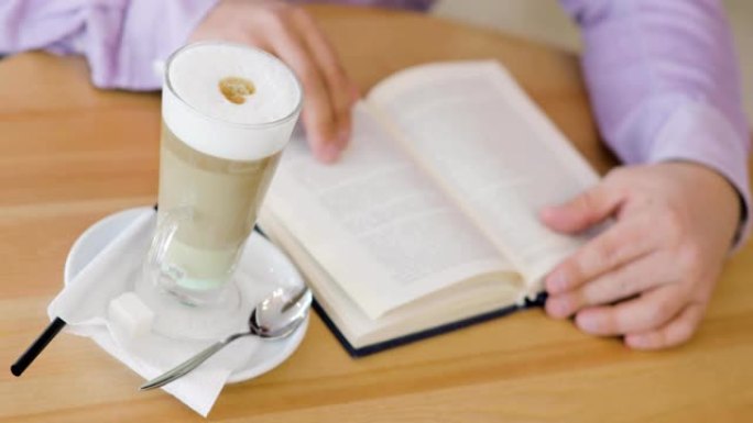 男人正拿着一杯卡布奇诺咖啡坐在咖啡馆里看书
