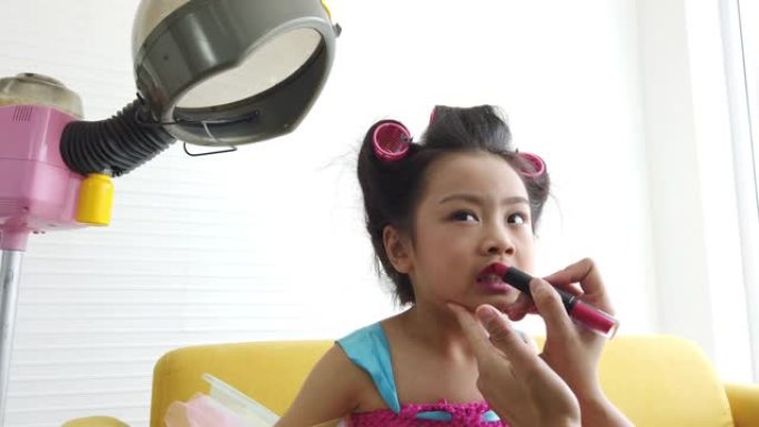 4k选择性聚焦中特写镜头的母亲的手用粉红色唇膏组成嘴唇，给卷头发坐在黄色沙发上的女儿。