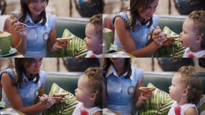 一位母亲和她的女婴坐在餐厅里分享一顿饭的肖像。儿童首次喂养的概念。