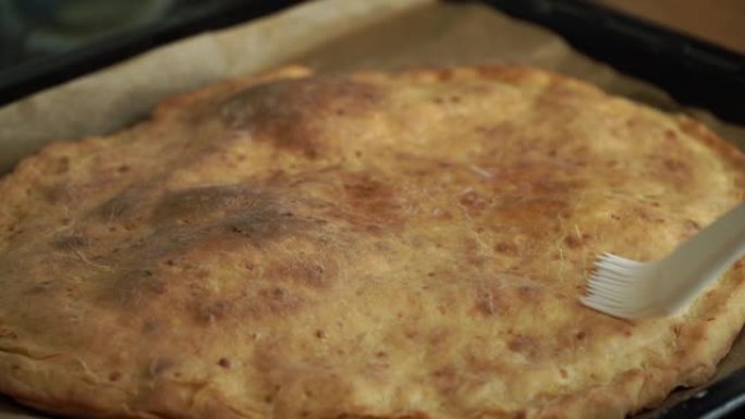 用刷子油在热烤的Khachapuri奶酪蛋糕上。特写。