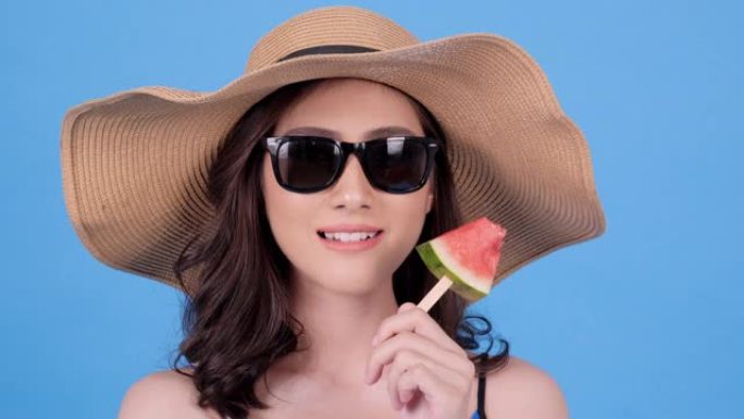 美丽的亚洲女人在蓝色背景下带着快乐的情感吃瓜。美丽，时尚和夏季概念。
