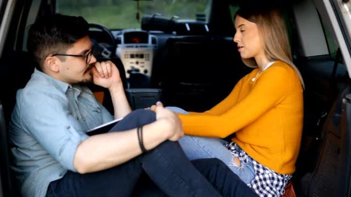 年轻夫妇坐在敞开的汽车后备箱里聊天