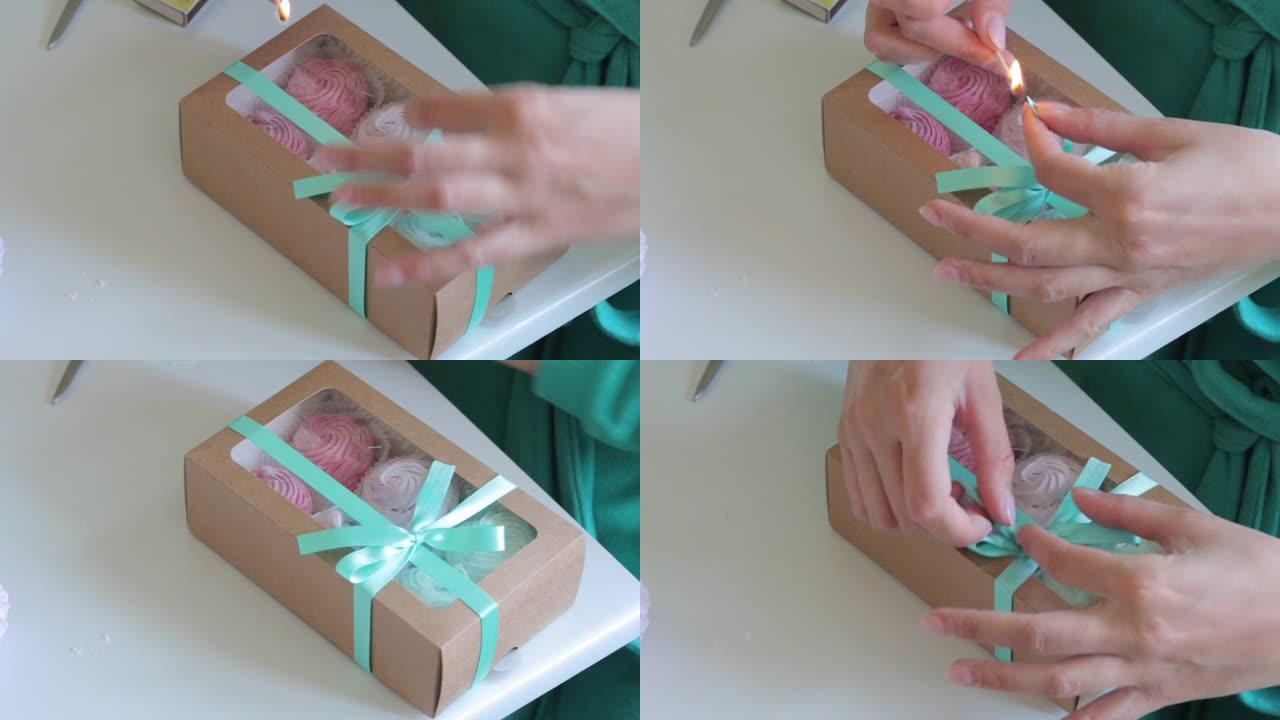 不同颜色的自制棉花糖装在礼品盒中。一名妇女用辫子绑了一个盒子，绑了一个蝴蝶结，并用火柴烧灼了丝带的末