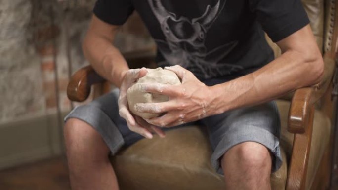 男艺术家坐在他的工作室里，用手揉捏粘土的底端照片。创造陶瓷产品概念。背景时尚研讨会