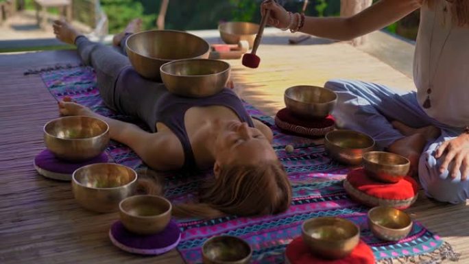 一位亚洲神圣医学大师的超级镜头为一位年轻女性表演了藏族碗治疗仪式。用藏族歌唱碗冥想。他们在凉亭里冥想