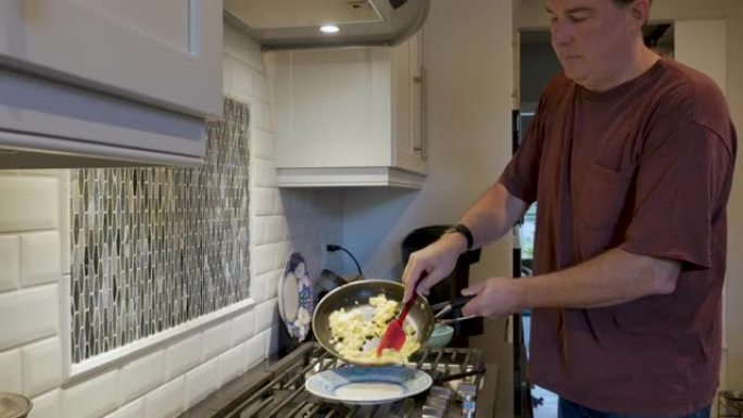 男子用硅胶刮刀将炒鸡蛋放在盘子上