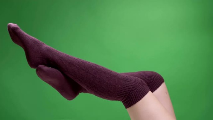 特写侧视图拍摄的女性少女腿穿着可爱的红色袜子轻轻地移动，背景孤立在绿色上