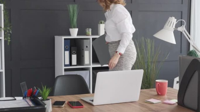 职场女性从书架上拿文件并在办公室使用笔记本电脑