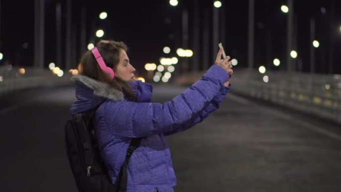女孩在夜镇的街道上散步时使用手机进行视频通话