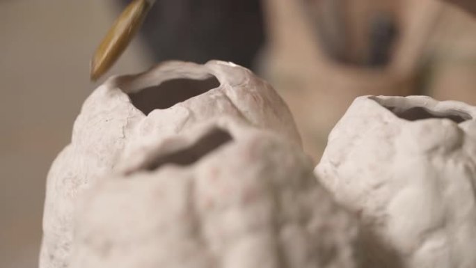 一个才华横溢的陶工的特写镜头，用刷子用液体物质覆盖现代风格的陶瓷雕塑。孤立，在模糊的背景上