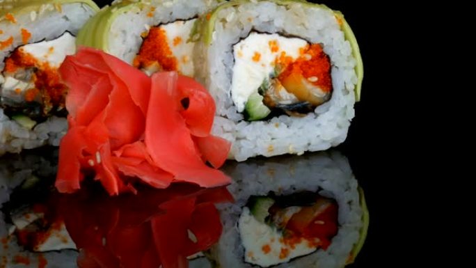 绿龙寿司卷和粉色姜。寿司卷配三文鱼、蔬菜和鳄梨特写。日本餐厅菜单在黑色背景下的镜面上