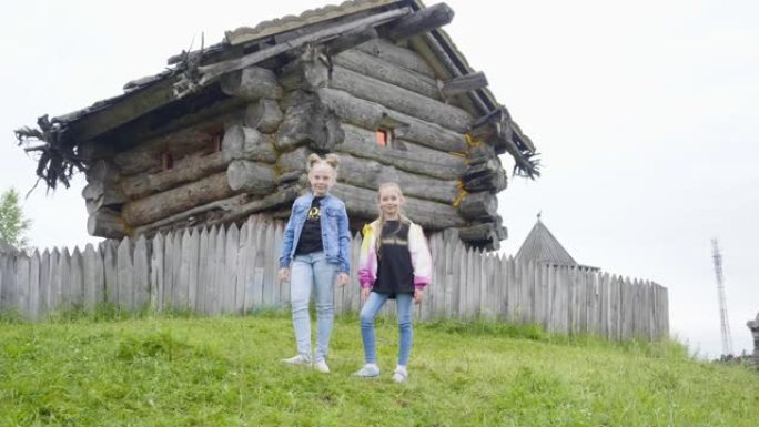 两个少女站在旋转的童话屋的绿色草坪上。十几岁的女孩在童话村老巫婆的木屋里摆姿势