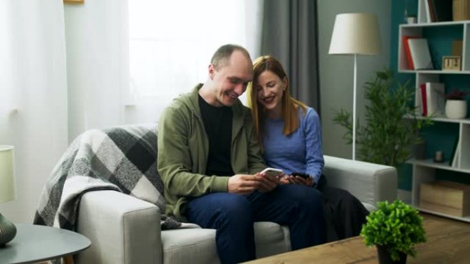 一对年轻夫妇在舒适的客厅里用智能手机观看有趣的视频