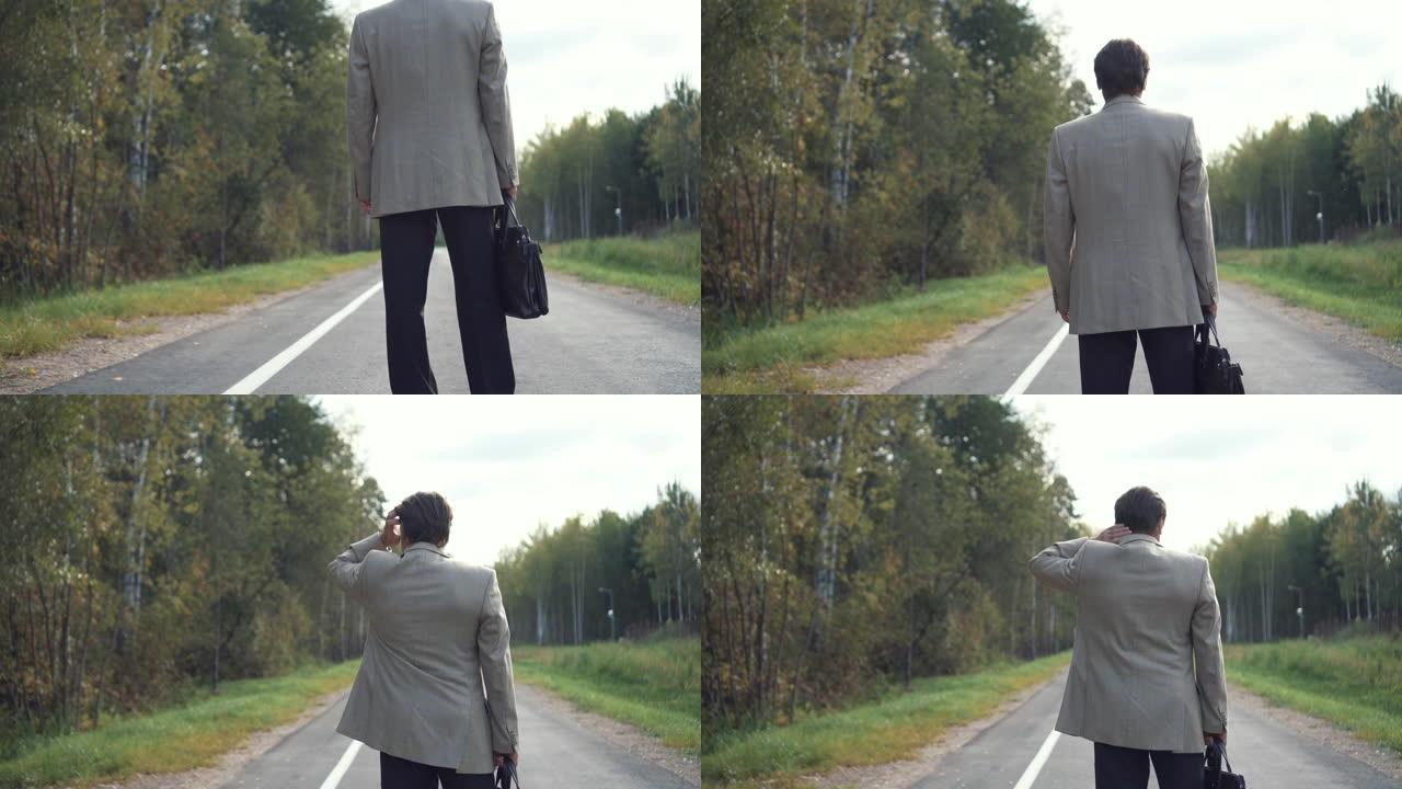 一位穿着公文包的夹克的老年商人正站在马路上，向远处望去。后视图。未知特征