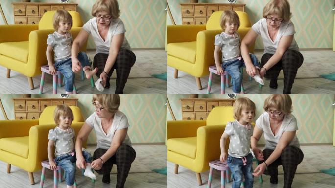 好看的祖母把婴儿袜子放在可爱的孙女小女孩的脚上，和她说话。婴儿护理